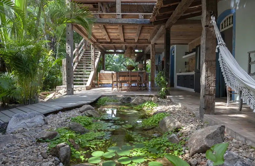 ma área de estar ao ar livre cercada por vegetação exuberante, com um pequeno lago decorativo e estrutura de madeira rústica.