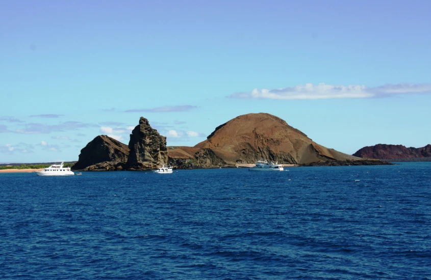 Ilha rochosa com barcos ao redor nas águas cristalinas das Ilhas Galápagos sob um céu azul claro