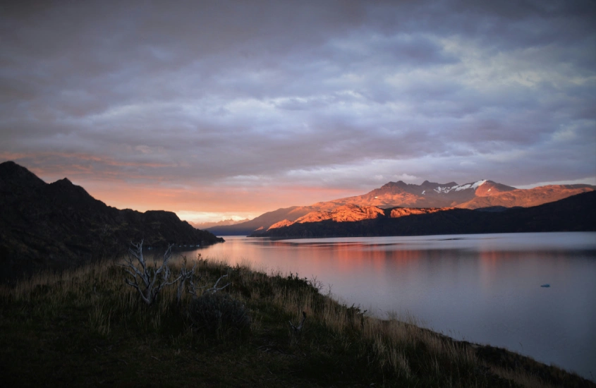 Pôr do sol iluminando as montanhas na Patagônia, com lago sereno ao lado