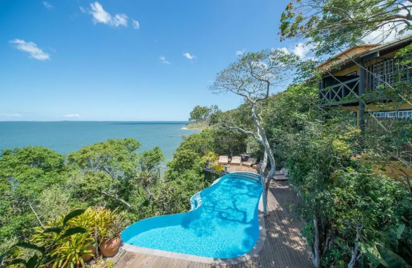 Uma piscina cercada por vegetação tropical, com vista para o mar e árvores ao redor, em um ambiente tranquilo e natural.