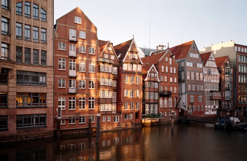 Fachada de edifícios históricos de tijolos refletindo na água ao pôr do sol em Hamburgo.