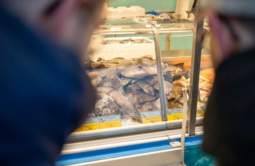 Duas pessoas observam uma vitrine repleta de peixes frescos e frutos do mar em um mercado.