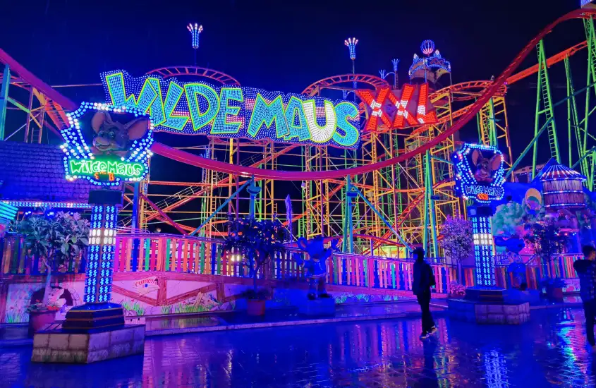 Estrutura de montanha-russa iluminada em cores vibrantes com o letreiro "Wilde Maus" em destaque.