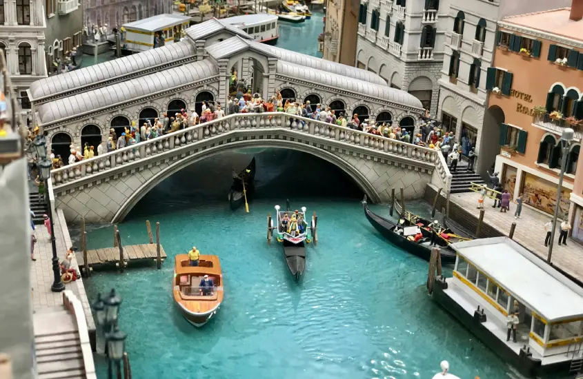 Réplica em miniatura da Ponte de Rialto em Veneza, com barcos e gôndolas navegando no canal.