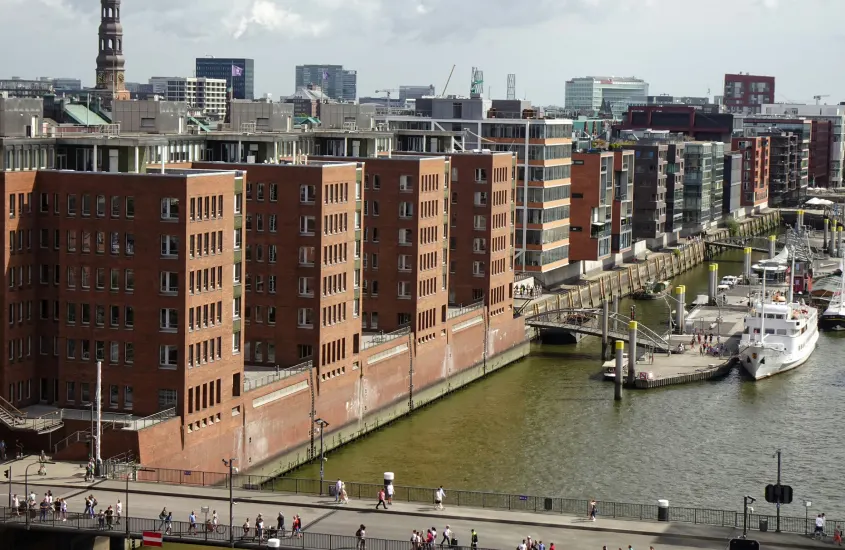 Vista aérea de prédios de tijolos ao longo de um canal com uma igreja e edifícios modernos ao fundo.