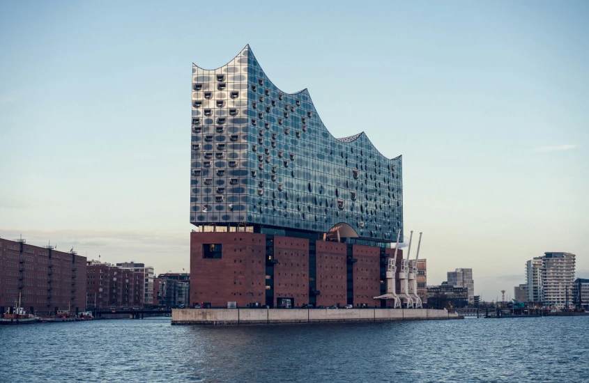 Fachada moderna de vidro da Elbphilharmonie, prédio icônico de Hamburgo, à beira do rio.