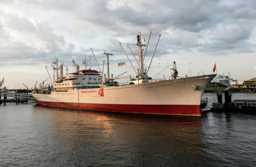 Navio Cap San Diego ancorado no porto de Hamburgo, com céu nublado ao fundo.