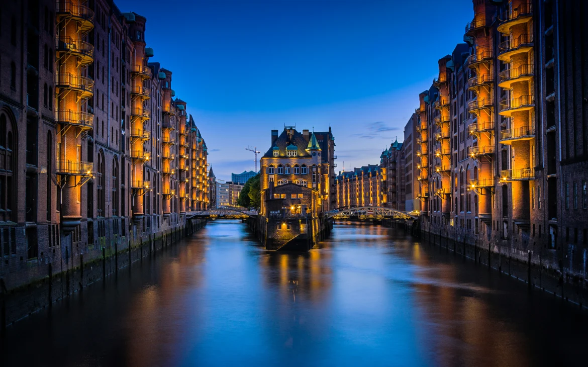 Vista noturna do canal Speicherstadt, com edifícios iluminados refletidos na água, criando uma cena encantadora