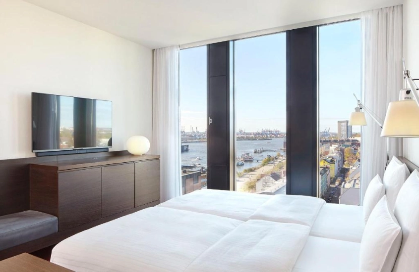 Quarto de hotel moderno com cama ampla e vista panorâmica para o porto de Hamburgo