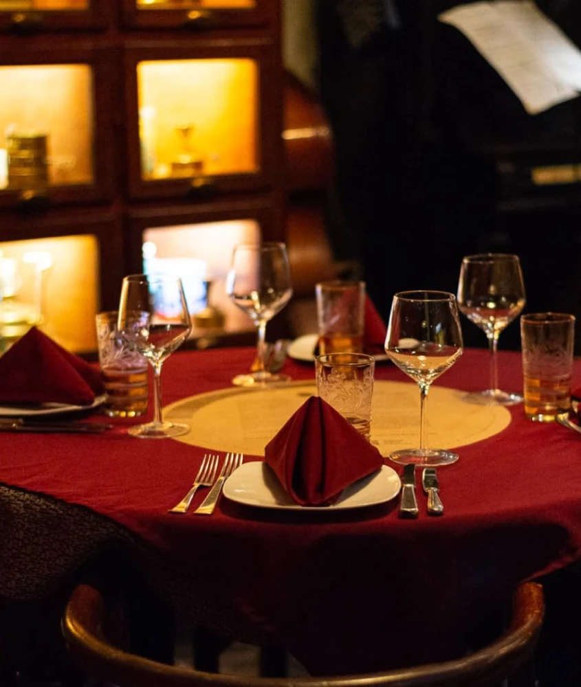 Mesa de jantar elegantemente arrumada com taças de vinho e guardanapos vermelhos no restaurante Primuseum, conhecido por suas apresentações de tango ao vivo