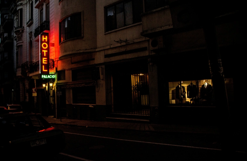 Fachada iluminada do Hotel Palácio à noite, com sua placa de neon em vermelho e amarelo destacando a entrada em uma rua tranquila no centro de Montevidéu