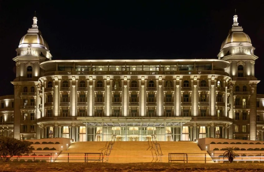 Fachada iluminada do luxuoso Sofitel Montevideo Casino Carrasco & Spa à noite, destacando sua arquitetura clássica e imponente, com cúpulas elegantes e um amplo terraço frontal