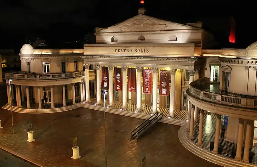 Fachada iluminada do Teatro Solís, com suas colunas e arquitetura clássica, um dos teatros mais antigos e importantes da América Latina, durante a noite em Montevidéu