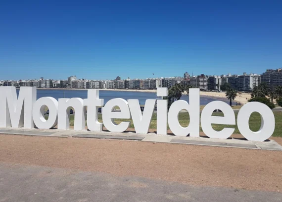 Letreiro icônico de Montevidéu em destaque à beira-mar, com prédios altos ao fundo e um céu azul claro, representando um dos pontos turísticos mais visitados da cidade