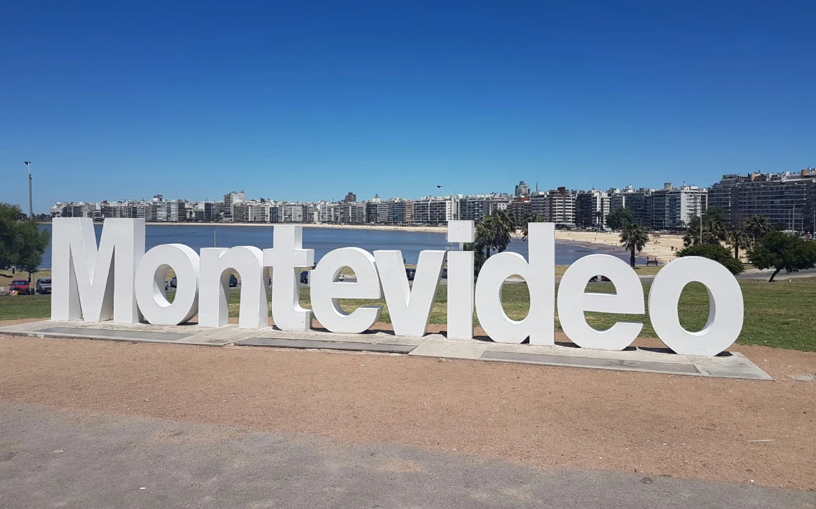 Letreiro icônico de Montevidéu em destaque à beira-mar, com prédios altos ao fundo e um céu azul claro, representando um dos pontos turísticos mais visitados da cidade