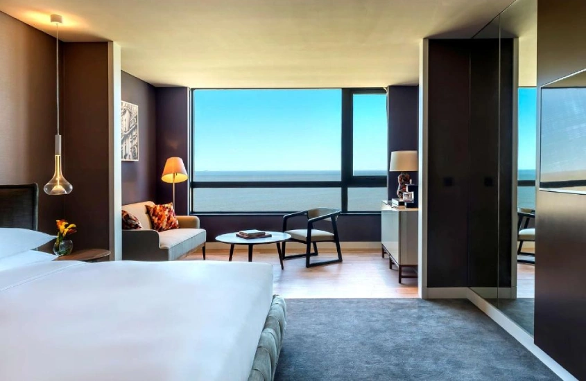 Quarto moderno e espaçoso do Hyatt Centric Montevideo, com amplas janelas que oferecem vista para o mar, proporcionando conforto e elegância