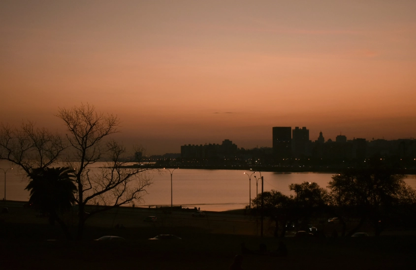 Pôr do sol suave sobre a cidade de Montevidéu, com as luzes da cidade se acendendo e o Rio da Prata refletindo o céu alaranjado