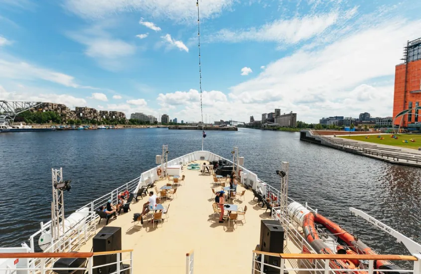 Vista de um barco turístico navegando pelo rio, oferecendo uma perspectiva relaxante de Montreal com o Habitat 67 ao fundo