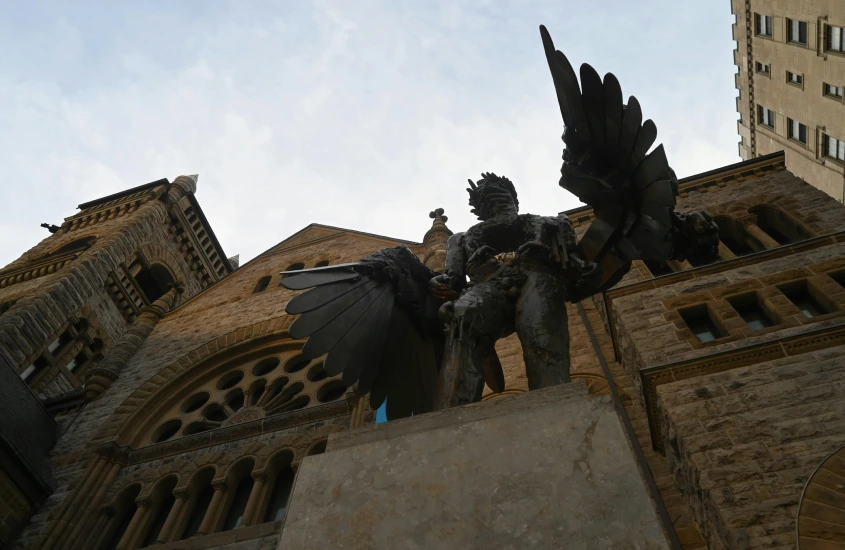 Estátua de um anjo de bronze com asas abertas em frente a uma igreja de pedra, uma escultura imponente no centro da cidade