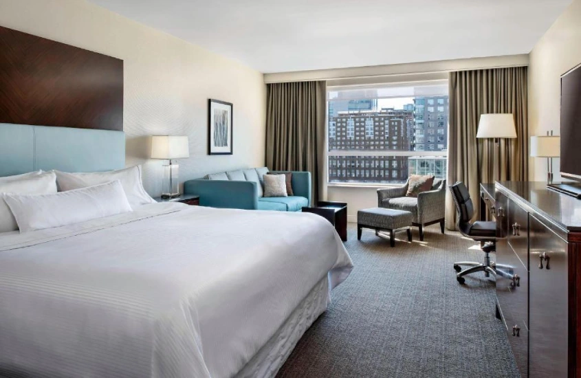 Quarto moderno e espaçoso do hotel Le Westin Montreal, com janelas amplas e vista urbana, oferecendo conforto e elegância no coração da cidade