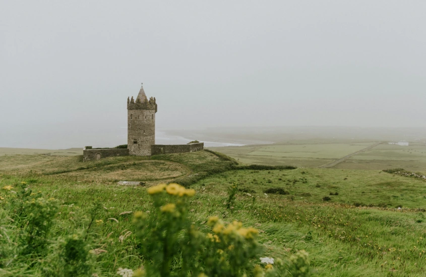 Torre medieval solitária rodeada por campos verdes e céu nebuloso na Irlanda, em uma paisagem tranquila e histórica