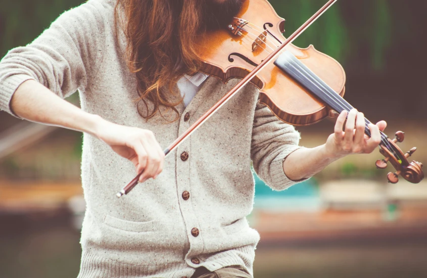 Músico tocando violino ao ar livre, com foco nas mãos e no instrumento