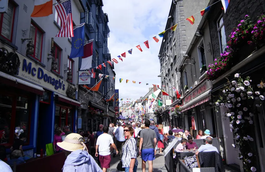 Rua repleta de pessoas e restaurantes com bandeiras penduradas, em Galway, Irlanda