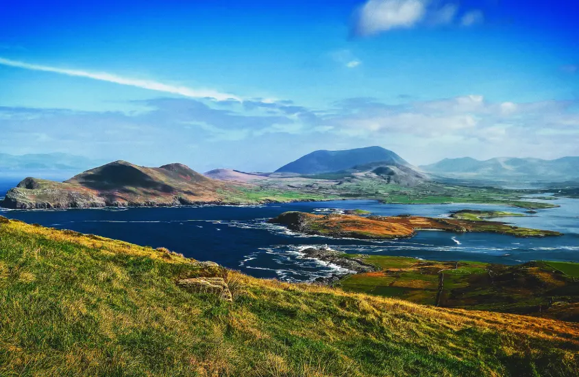 Vista panorâmica das montanhas e do litoral verdejante da Irlanda, cercado por águas cristalinas e céu azul brilhante