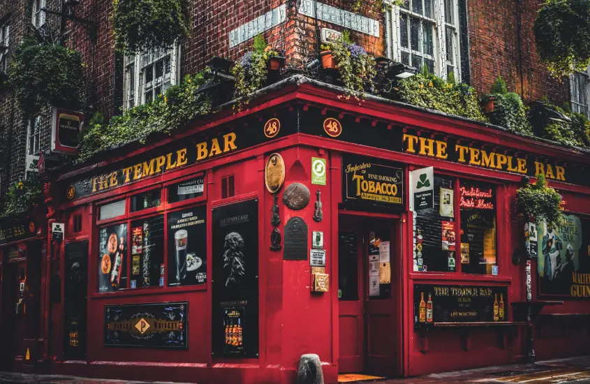 Fachada icônica do Temple Bar, famoso pub localizado em Dublin, com exterior vermelho e plantas decorativas