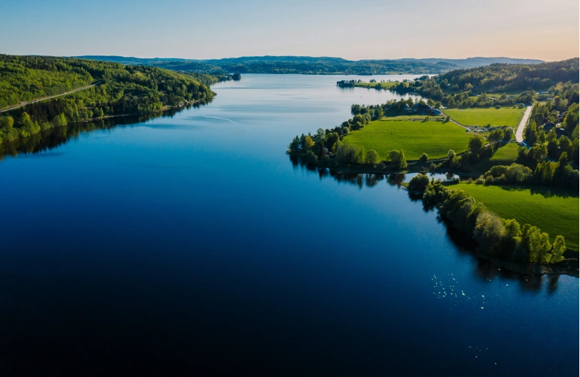 Paisagem serena de um lago na Suécia cercado por colinas verdes sob o céu claro de verão