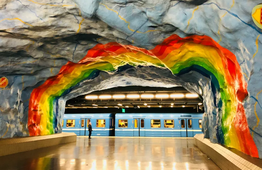 Estação de metrô colorida em Estocolmo com arte em forma de arco-íris nas paredes rochosas.