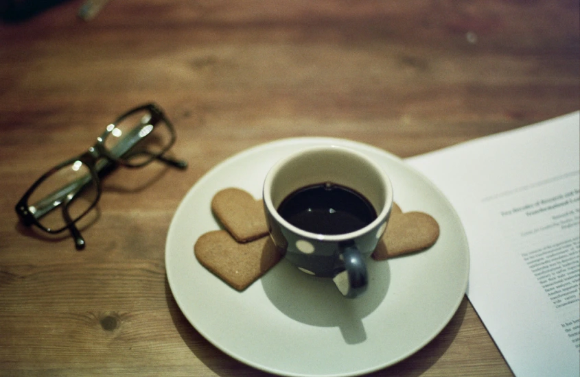 Xícara de café preto ao lado de biscoitos em forma de coração, símbolo do tradicional Fika sueco.