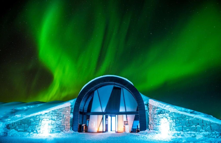 Hotel de gelo na Suécia iluminado pela aurora boreal em uma noite de inverno.