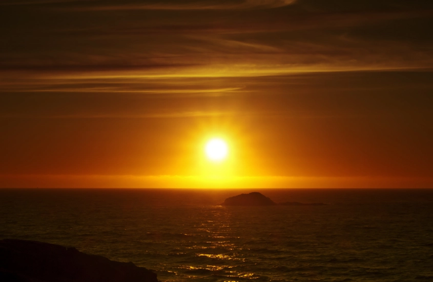 Pôr do sol dourado sobre o oceano visto da costa sueca, com uma pequena ilha ao fundo.