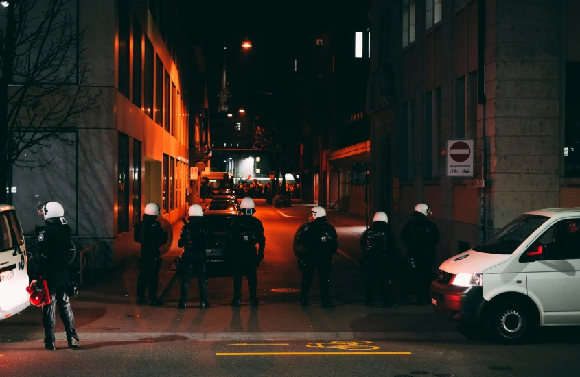 Grupo de policiais em fila em uma rua escura de uma cidade, prontos para intervenção noturna