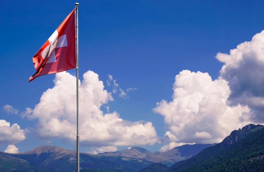 Bandeira suíça tremulando contra o céu azul com montanhas ao fundo