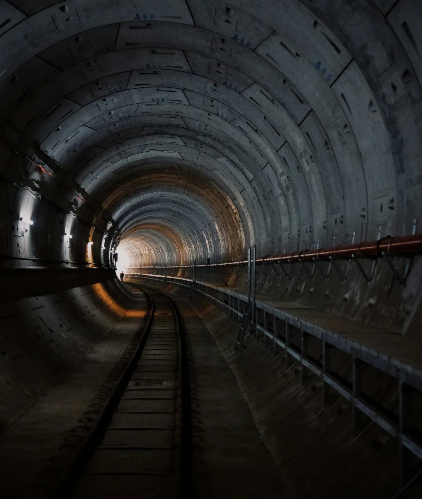 Vista interna de um túnel ferroviário de concreto, iluminado por luzes