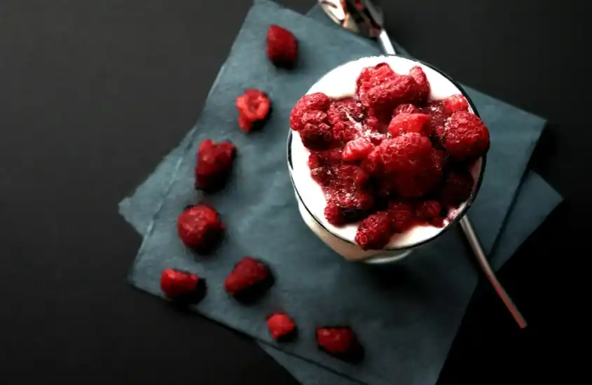 Sobremesa com iogurte e frutas vermelhas, acompanhada de uma colher sobre um guardanapo escuro