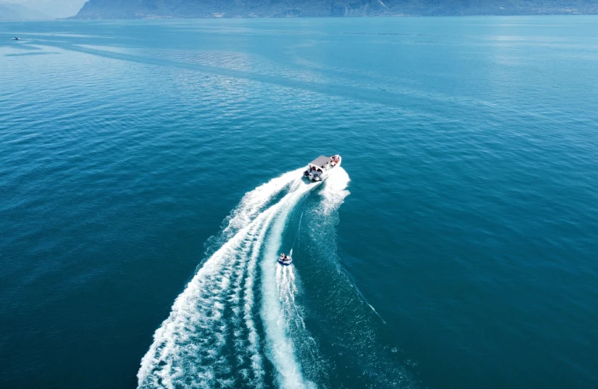 Barco navegando em um lago azul com montanhas ao fundo, deixando um rastro de ondas na água