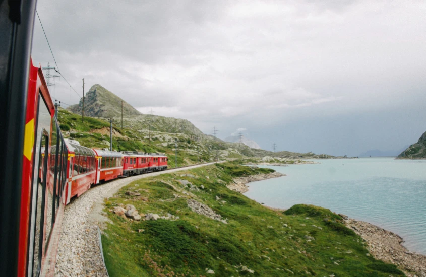 Trem vermelho percorrendo a paisagem montanhosa dos Alpes Suíços, próximo a um lago azul claro