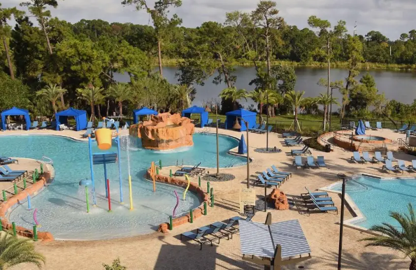 Vista da piscina do Wyndham Lake Buena Vista Disney Springs Resort Area, cercada por palmeiras, cadeiras de sol e guarda-sóis coloridos.