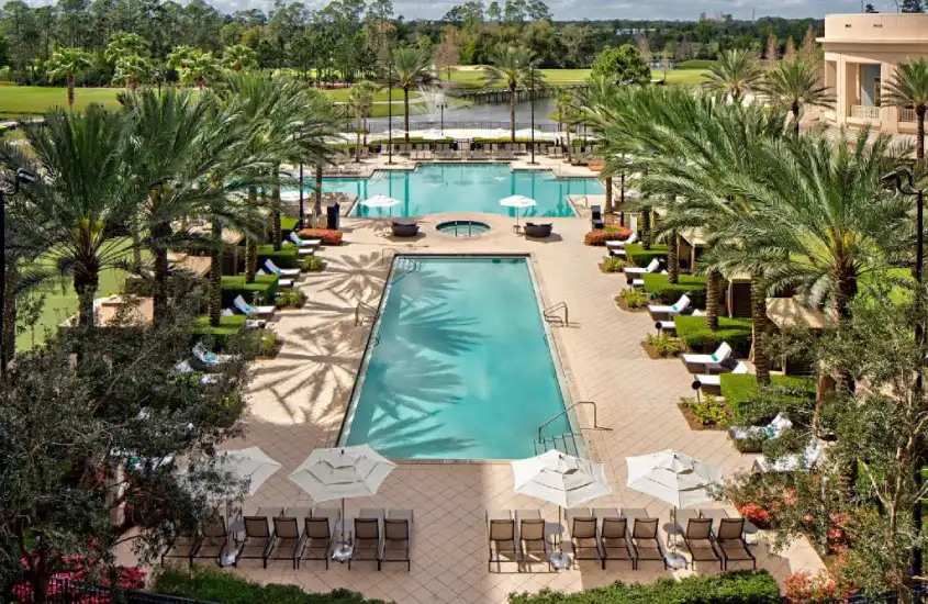 Vista aérea da área de piscinas no Waldorf Astoria Orlando, com palmeiras e cadeiras de sol em um ambiente elegante.