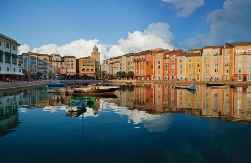 Fachada colorida e vibrante do Universal's Loews Portofino Bay Hotel, com inspiração italiana e barcos flutuando no lago ao redor.