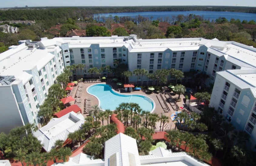 Vista aérea da piscina do Holiday Inn Resort Orlando Lake Buena Vista cercada por palmeiras e espreguiçadeiras, com o lago ao fundo.