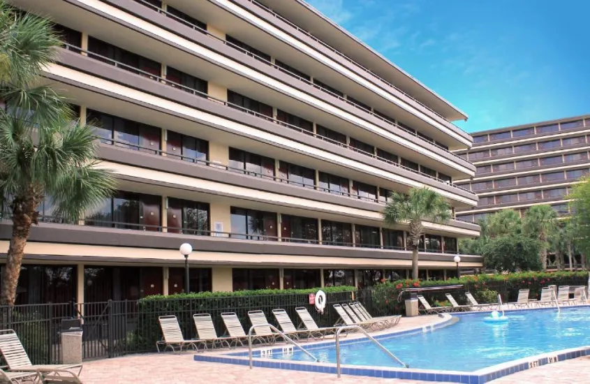 Vista frontal do Rosen Inn at Pointe Orlando, com piscina externa e fachada de vários andares rodeada de palmeiras.