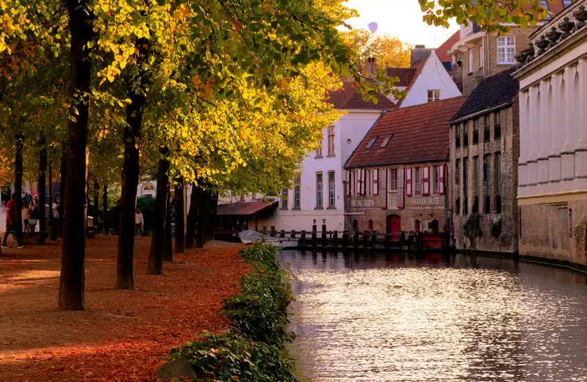 Canal em Bruges, Bélgica, cercado por casas históricas e árvores com folhagem amarelada, em um cenário de outono