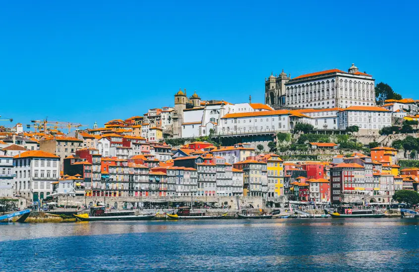 Vista panorâmica do centro histórico do Porto, com suas casas coloridas de telhados laranja e a Sé do Porto ao fundo, à beira do Rio Douro