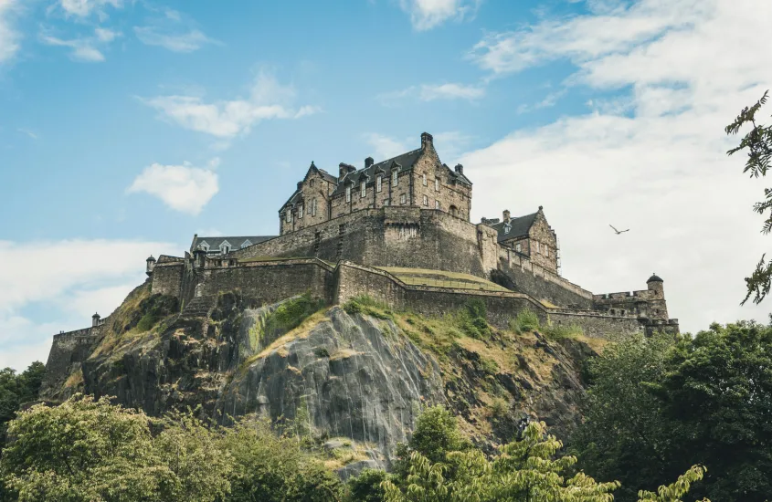 O Castelo de Edimburgo, construído no topo de um penhasco rochoso, com suas paredes de pedra imponentes e céu azul ao fundo