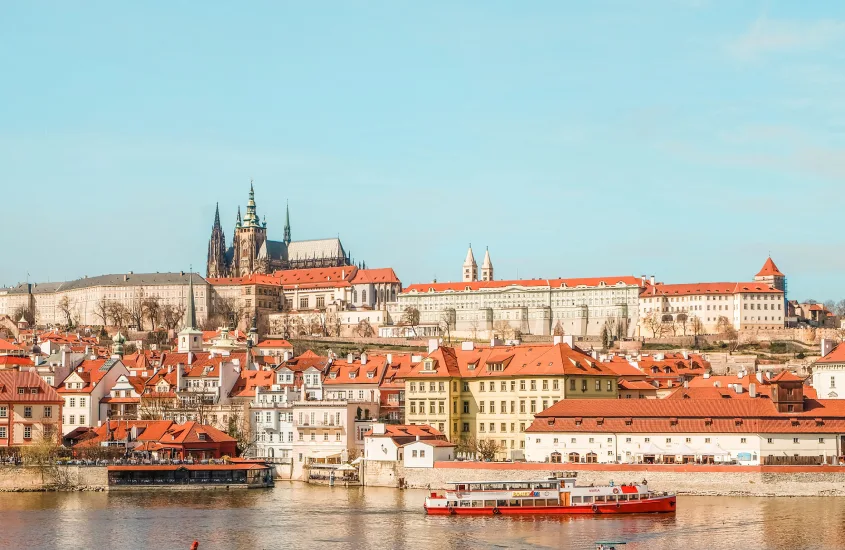 Uma vista do Castelo de Praga, com telhados vermelhos e edifícios históricos às margens do Rio Vltava