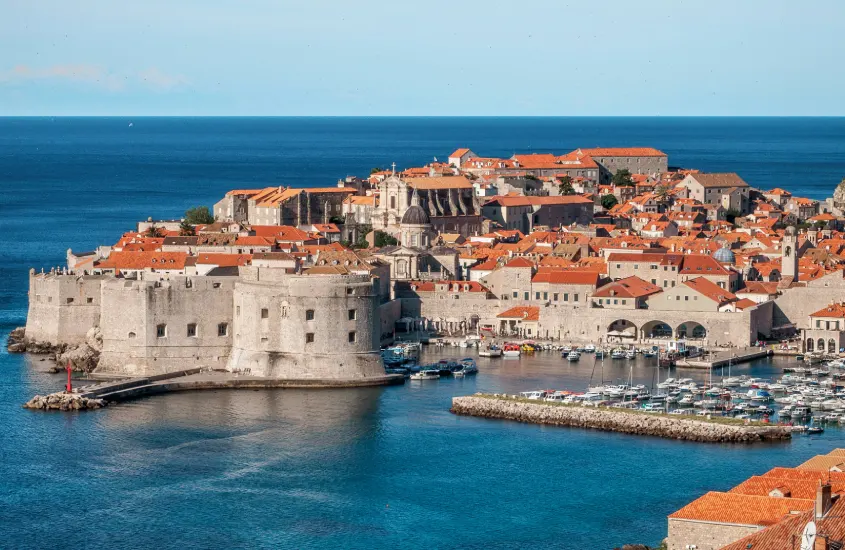 Cidade de Dubrovnik, Croácia, com suas muralhas históricas e telhados alaranjados, banhada pelo Mar Adriático